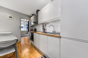 a kitchen with white cabinets and a wooden floor at Main Street Corner Great 1bedroom Flat - Richmond in London