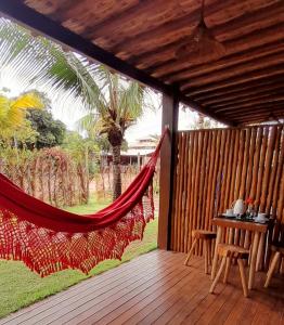 a hammock on a wooden deck with a table and a palm tree at D'Ajuda Flat Taipu Bangalôs in Taipu