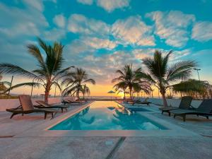 uma piscina na praia com palmeiras e um pôr do sol em Kavalá em San Blas