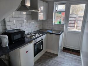 a small kitchen with a stove and a microwave at Bethel- beautiful new 1 bed house near Erith station in Erith