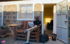a man sitting on a chair reading a book at Perfect Travel-Stop Room 3Km From Nanyuki Town - Charell View in Nanyuki