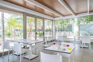 een restaurant met witte tafels, stoelen en ramen bij Hotel Roquetas El Palmeral by Pierre & Vacances in Roquetas de Mar