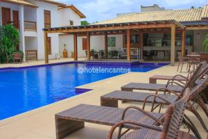 a resort with a swimming pool with chairs and a house at Encantos de Itaperapuã in Porto Seguro