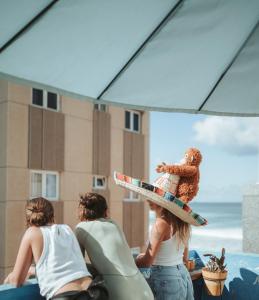 a woman with a surfboard and a doll on her head at La Ventana Azul Surf Hostel in Las Palmas de Gran Canaria