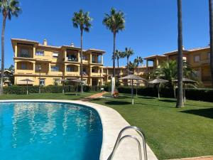einem Pool vor einem Gebäude mit Palmen in der Unterkunft Apartamento excelente ubicación en Novo Sancti Petri By Chiclana Dreams in Chiclana de la Frontera