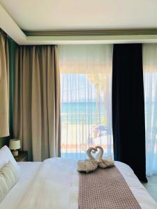 due asciugamani da cigno su un letto di fronte a una finestra di SunRose Beach Aparthotel ad Acharavi