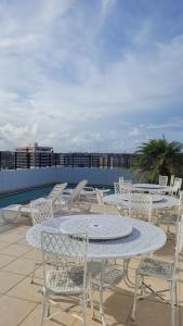 a patio with white tables and chairs on a roof at Apartamento Pajuçara in Maceió