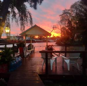 a wooden deck with a gazebo and chairs at sunset at Cabañas Burdeos in Tigre
