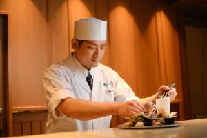 Ein Mann in einem Kochhut, der einen Teller mit Essen zubereitet. in der Unterkunft Onomichi Hansei in Onomichi