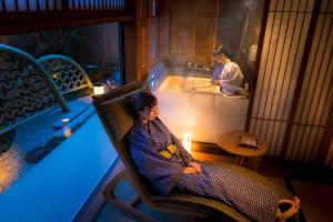 une femme assise sur une chaise à côté d'une baignoire dans l'établissement Onomichi Hansei, à Onomichi