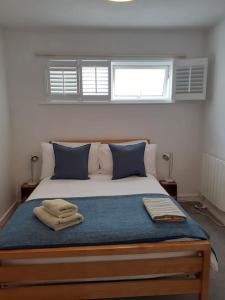a bedroom with a bed with blue pillows and two windows at Wheelers Bay Apartment in Ventnor