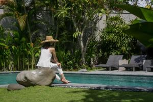 Eine Frau, die auf einem Felsen neben einem Pool sitzt in der Unterkunft The Amala Boutique Retreat in Seminyak