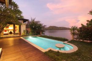 a swimming pool in front of a house with a lake at Lombok Sunset Bay Resort in Sekotong