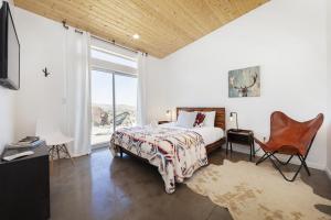 een slaapkamer met een bed, een stoel en een raam bij Rock Box - Modern Adobe Nestled in the Boulders Above Coyote Hol home in Joshua Tree
