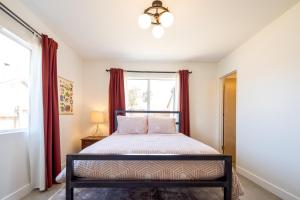 a bedroom with a bed with red curtains and a window at The RockHopper - Hot Tub, Fire Pit & Walk to Downtown JT! home in Joshua Tree