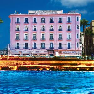 Le Metropole Luxury Heritage Hotel Since 1902 by Paradise Inn Group في الإسكندرية: مبنى وردي على شاطئ الماء