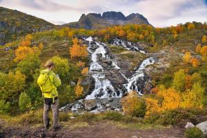 un homme dans une veste jaune debout devant une cascade dans l'établissement Lofoten Planet BaseCamp, à Sørvågen