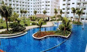 a large blue swimming pool with palm trees and a building at Shore 1 Residences MOA Staycation in Manila