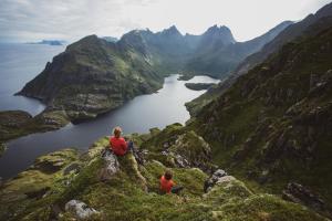 2 personnes assises au bord d'une montagne surplombant un lac dans l'établissement Lofoten Planet BaseCamp, à Sørvågen