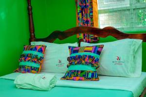 Richy Hotels and Safaris في Mbale: سرير مع الوسائد الملونة والجدار الأخضر