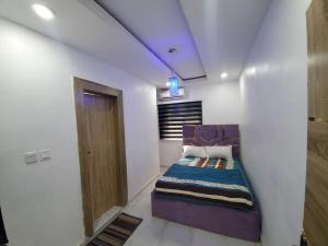Un dormitorio con una cama morada en una habitación blanca en Dinero Rose-2 Bedroom Apartment, en Lagos