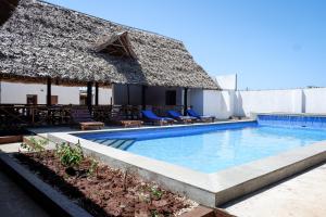 a swimming pool with chairs and a thatched building at Nungwi Heritage Resort in Nungwi