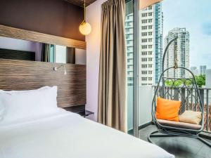 a bedroom with a bed and a chair and a window at Mercure Singapore Tyrwhitt in Singapore