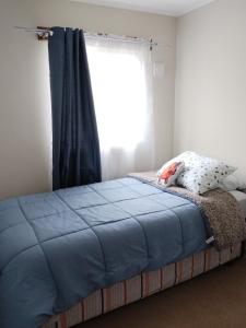 a bed with a blue blanket and a window at Departamento familiar en Osorno in Osorno