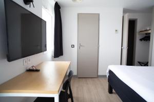 a bedroom with a bed and a desk with a flat screen tv at Hôtel Les Genêts Bayonne in Bayonne