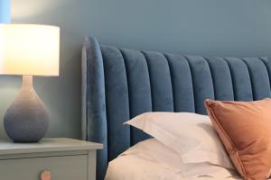 a bed with a blue headboard next to a table with a lamp at STYLISH, BEACHSIDE apartment, sea views in St Merryn