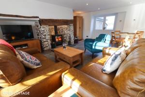 a living room with a leather couch and a fireplace at Cobb Cottage - HiddenDevon in Winkleigh