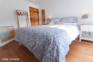 a bedroom with a bed with a blue and white comforter at Cobb Cottage - HiddenDevon in Winkleigh