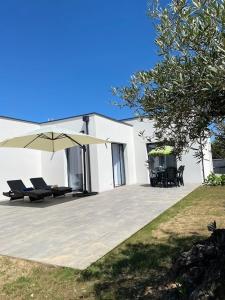 ein weißes Haus mit einer Terrasse mit Sonnenschirm in der Unterkunft new architect villa with large terrace and patio 800 m from the sea in Vaux-sur-Mer
