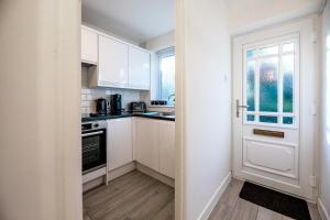 a small kitchen with white cabinets and a door at Haygarth Apartment in Knebworth