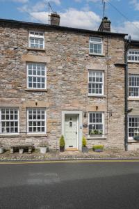 - un bâtiment en pierre avec une porte blanche et des fenêtres dans l'établissement Weavers Cottage, Sleeps 4, town centre, à Kirkby Lonsdale