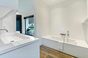 ein weißes Badezimmer mit einem Waschbecken und einem Spiegel in der Unterkunft d'Oude Schaapskooi, de luxe vakantiehoeve in Damme in Damme
