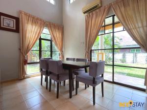 a dining room with a table and chairs and windows at Afamosa Villa with private pool by BeeStay in Kampong Alor Gajah
