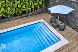a swimming pool with an umbrella and two chairs at Casa El Paraiso - Private Pool, Jacuzzi, Air-con and BBQ By Lanzarote Vacation Homes in Tías