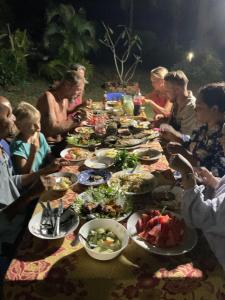 een groep mensen die rond een lange tafel zitten met borden eten bij Mada Lanta Mai Keaw in Koh Lanta