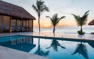 a resort swimming pool with palm trees and the ocean at Bella Villa in Tulum