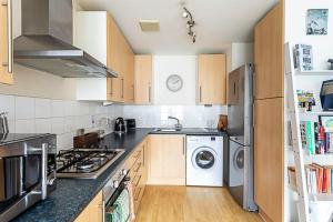 Bright Flat in Historic Whitechapel في لندن: مطبخ بدولاب خشبي وغسالة ومجفف