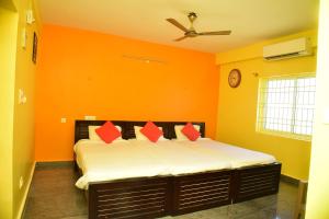 Schlafzimmer mit orangefarbenen Wänden und einem Bett mit roten Kissen in der Unterkunft SAI SADHAN RESIDENCY in Chittoor