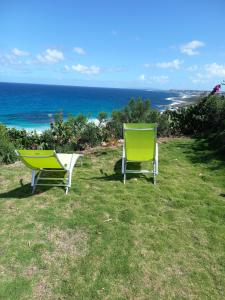 two green and white chairs sitting on the grass near the ocean at La Marine in Le Moule