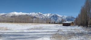 un campo cubierto de nieve con una cabaña frente a las montañas en FINCA LA PAZ en Uspallata