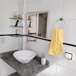 La salle de bains est pourvue d'un lavabo blanc et d'un miroir. dans l'établissement Apto Enseada, 2 quadras da praia - 2 quartos com ar condicionado - 6 hospedes, à Guarujá
