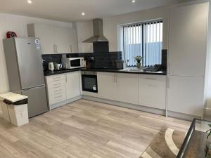 a large kitchen with white cabinets and a refrigerator at Evergreen Lodge - Two Bed Lux Flat - Parking, Garden, Patio, WIFI, Netflix - Close to Blenheim Palace & Oxford - F3 in Kidlington