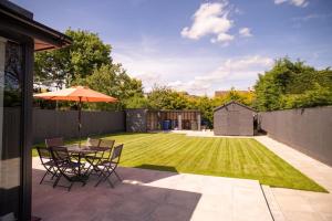 基德靈頓的住宿－Rosey Lodge - One Bed Cousy Flat - Parking, Netflix, WIFI - Close to Blenheim Palace & Oxford - F5，庭院设有带雨伞的桌子和草坪。
