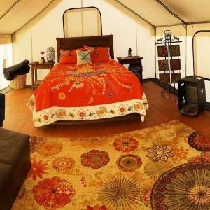 a bedroom with a bed with an orange comforter and a rug at Cozy Glamp Tents at Wildland Gardens in Joseph