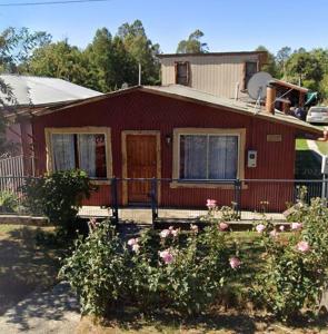 a red house with a porch and flowers in front of it at Cabaña con estacionamiento in Panguipulli