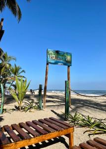 ein Schild am Strand mit einer Holzbank in der Unterkunft Palmarío Hostal in Guachaca